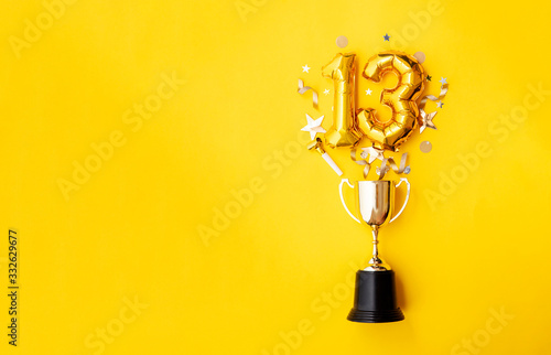 Number 13 gold anniversary celebration balloon exploding from a winning trophy