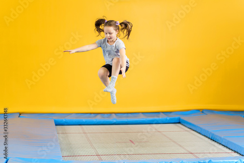 Happy little girl jumping on trampoline in fitness center