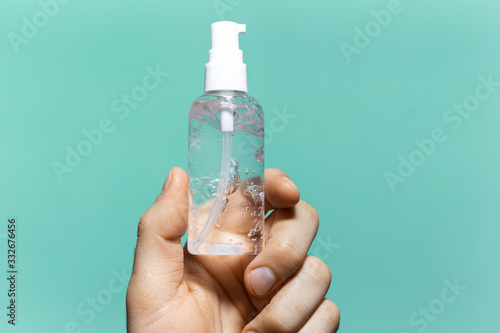 Close-up of male hand holding small plastic bottle of sanitizer antibacterial gel on background of cyan aqua menthe color.