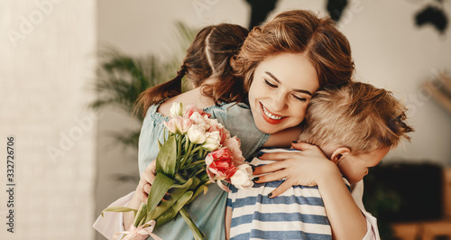 Little children congratulating and hug mother in kitchen.