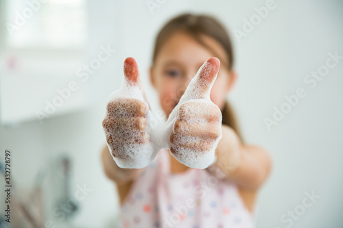 Little girl washing hands with water and soap in bathroom. Kid showing thumbs up. Hands hygiene and virus infections prevention. 