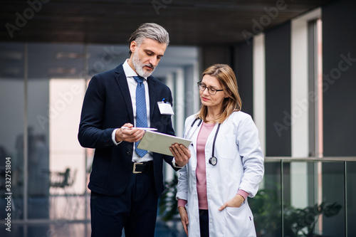 Pharmaceutical sales representative with tablet talking to doctor.