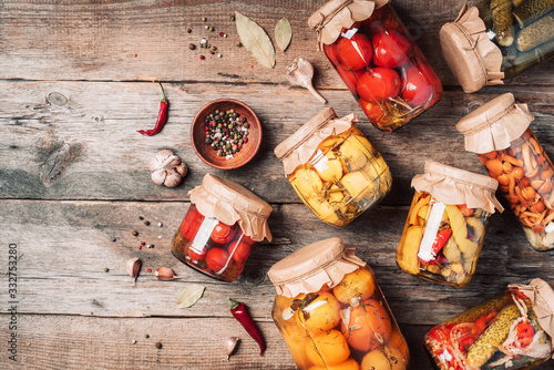 Canned and preserved vegetables in glass jars over wooden background. Top view. Flat lay. Copy space.