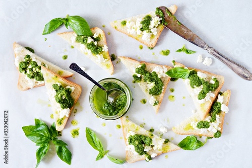 Crispy toasts (crostini, bruschetta) with cottage cheese (ricotta) and freshly prepared pesto. Homemade basil pechto sauce in a jar on a light background.
