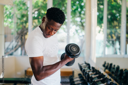 Young African American man standing and lifting a dumbbell with the rack at gym. Male weight training person doing a biceps curl in fitness center