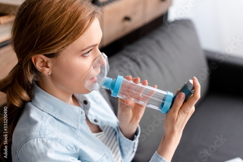 asthmatic woman using inhaler with spacer in living room