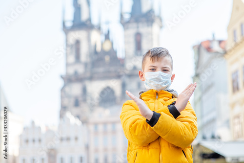 Portrait of a boy wearing medical mask stands on the old town square in Prague and shows stop gesture. Coronavirus epidemic concept