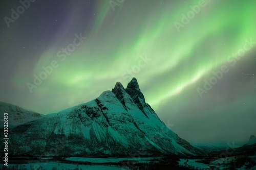 Otertinden peak in Norway, under the northern lights Beautiful mountains through Arctic Norway, with the Auroras dancing on top. Lyngen Alps Scandinavia. Mountain which is covered with snow. 