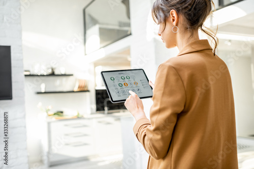 Woman controlling smart home devices using a digital tablet with launched application in the white living room. Smart home concept