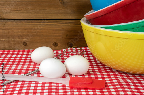 stack of retro mixing bowls on checkered tablecloth with white eggs and kitchen utensils