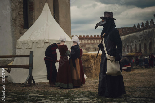 A masquerade historical scene reconstruction. Plague doctor in medieval old town. Castle and epidemic