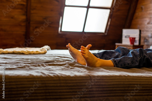 horizontal close-up photo of bare feet on a bed in a country house against the roof window