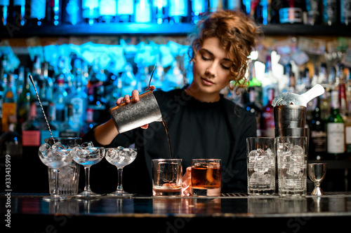Young woman barman preparing cocktail and pouring it into glass.