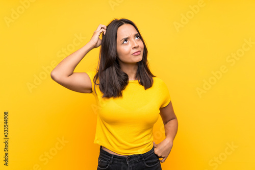 Young brunette girl over isolated background having doubts while scratching head