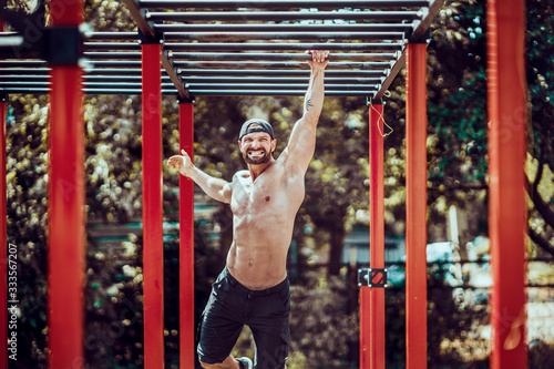 Bearded bodybuilder man exercising on monkey bars for the upper-body in a modern calisthenics park outdoors on a sunny day.