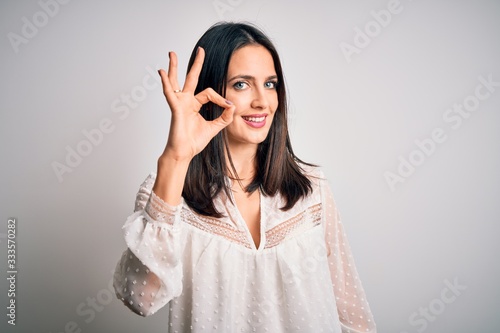 Young brunette woman with blue eyes wearing casual t-shirt over isolated white background smiling positive doing ok sign with hand and fingers. Successful expression.