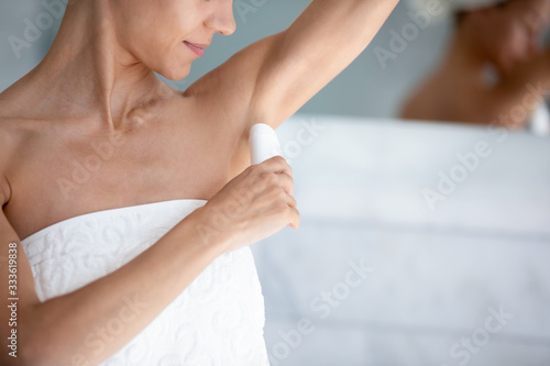 Happy 30s beautiful woman applies antiperspirant stick after shower in morning close up image. Using treatment for bodycare skincare, to reduce sweating, underarm wetness and control body odor concept