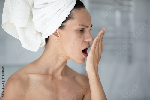 Woman with towel on head put palm in front face opens mouth check breath close up image. Suffers from unpleasant odor due to oral infections, poor dental hygiene, health problems, halitosis concept