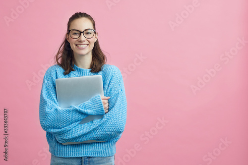 Cute looking student holding her laptop beside copy space 