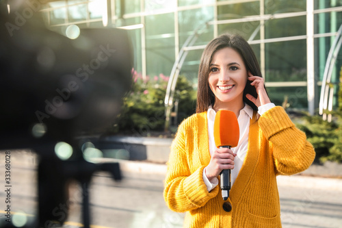 Young female journalist with microphone working on city street