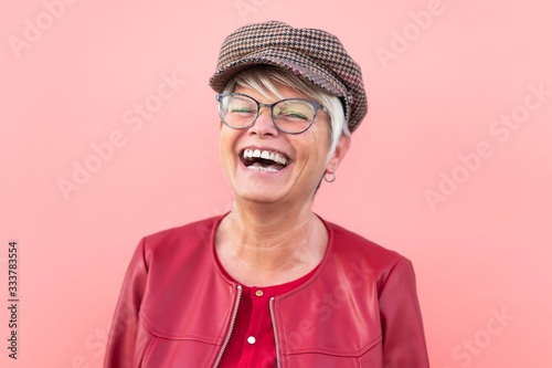 Happy senior woman having fun outdoor - Trendy mature person laughing and enjoying retired time - Elderly people lifestyle and mother's day concept - Coral Background