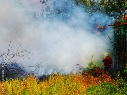 Fireman using water and extinguisher to fighting with fire flame in an emergency situation.,There is dirty smoke floating over the area.