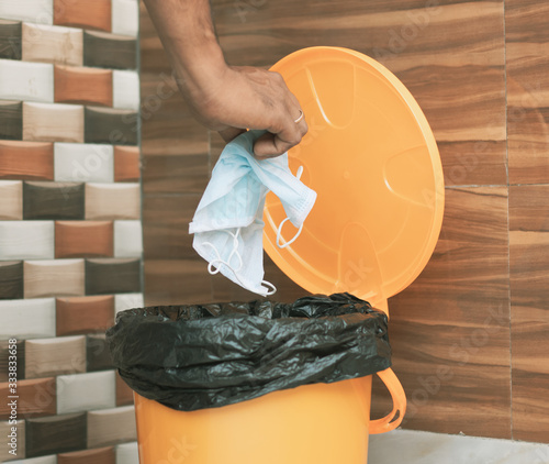 Hands throwing medical mask into closed bin - Covid-19, Coronavirus advice to discard or dispose medical mask to closed trash can after usage - concept showing to do hygiene practice.