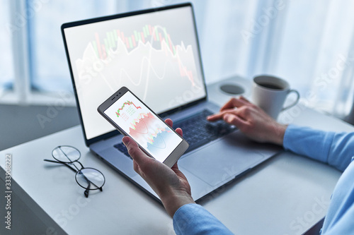 Modern business woman investor analyzes and watches a changing chart of stock trade and exchange money market on computer and smarthphone at workplace