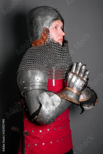 A young knight in medieval armor prays with his hands clasped.