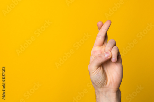 fingers crossed hope sign. close up man hand symbolising faith against yellow background
