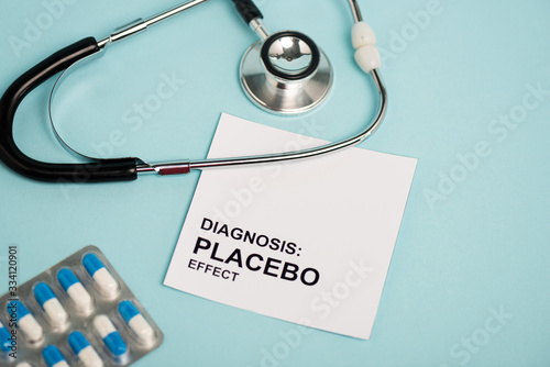 Card with placebo effect lettering, pills and stethoscope on blue background