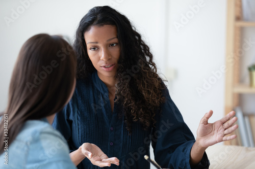 Concentrated african American businesswoman talk with female colleagues brainstorm consider project at meeting, focused woman employee speak discuss business ideas with coworker at office briefing