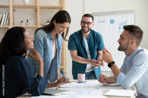 Smiling diverse colleagues gather in boardroom brainstorm discuss financial statistics together, happy multiracial coworkers have fun cooperating working together at office meeting, teamwork concept