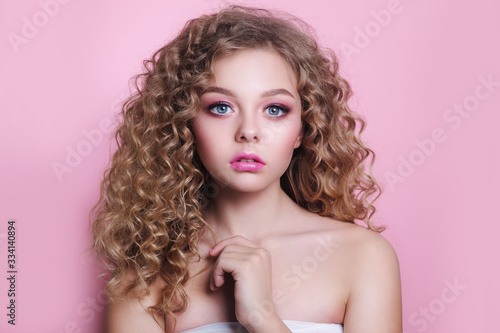 blonde girl with long and shiny curly hair . Beautiful model woman with wavy hairstyle on pink background