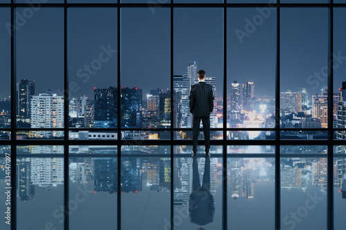 Businessman standing in modern office interior and looking to night city