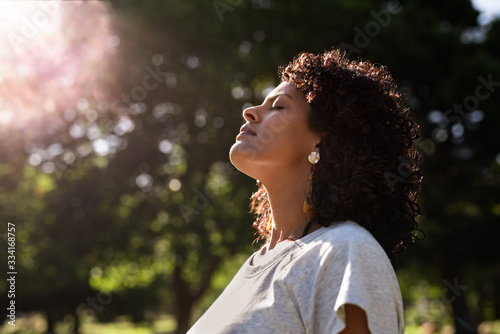 Young woman standing outdoors feeling the sun on her face