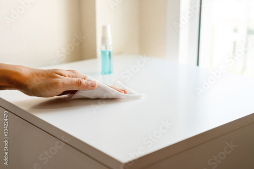 Woman hand cleaning headboard with disinfectant wet wipe and alcohol spray in bedroom at home. Concept of disinfecting surfaces from bacteria or viruses. Close up