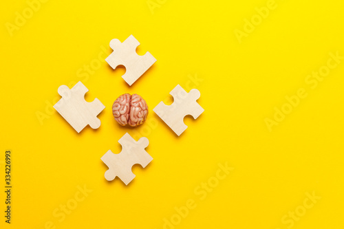 Human brain with a puzzle on yellow background. Business idea, memory loss, training and new skills.