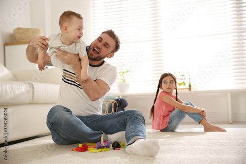 Unhappy little girl feeling jealous while father spending time with her baby brother at home