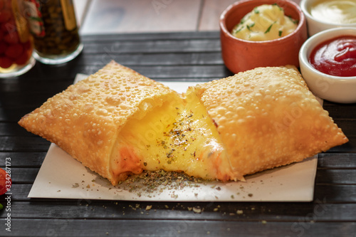 Pastel de quatro queijo com cheddar e mussarela e catupiri e gorgonzola e parmesão em uma mesa com uma esteira preta e guardanapo com fundo de molho 