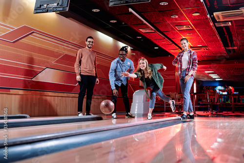 Pretty young female throwing bowling ball on track during play with friends