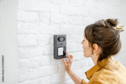 Woman rings the house intercom with a camera installed on the white brick wall