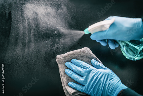 Surface home cleaning spraying antibacterial sanitizing spray bottle disinfecting against COVID-19 spreading wearing medical blue gloves. Sanitize surfaces prevention in hospitals and public spaces.