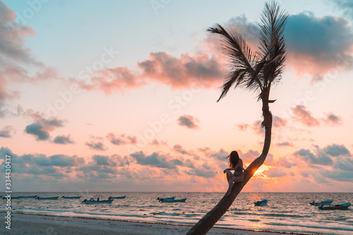 Girl sitting on a palm tree at sunrise on the sandy beach of the Caribbean i