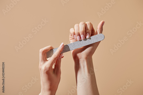 Partial view of woman filing fingernails with emery board isolated on beige