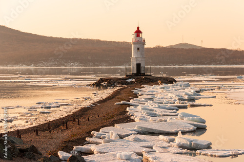 The famous Tokarevsky lighthouse on the Egersheld peninsula in Vladivostok on a winter morning at dawn among ice floes floating in the sea.