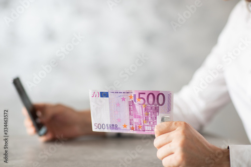 Banknot o nominale 500 Euro trzymany w ręce, bizmesmen piszący na telefonie. Waluta € i nominał pięćset.