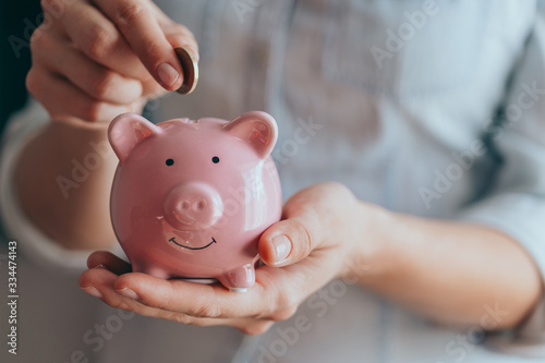 female hands hold a pink piggy bank and puts a coin there. The concept of saving money or savings, investment