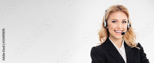Portrait of happy smiling young support phone operator or confident businesswomen in headset, over grey background, with blank copy space area for slogan or text message.