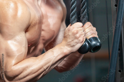 Close up of strong muscular man training his triceps using sport equipment in the modern gym